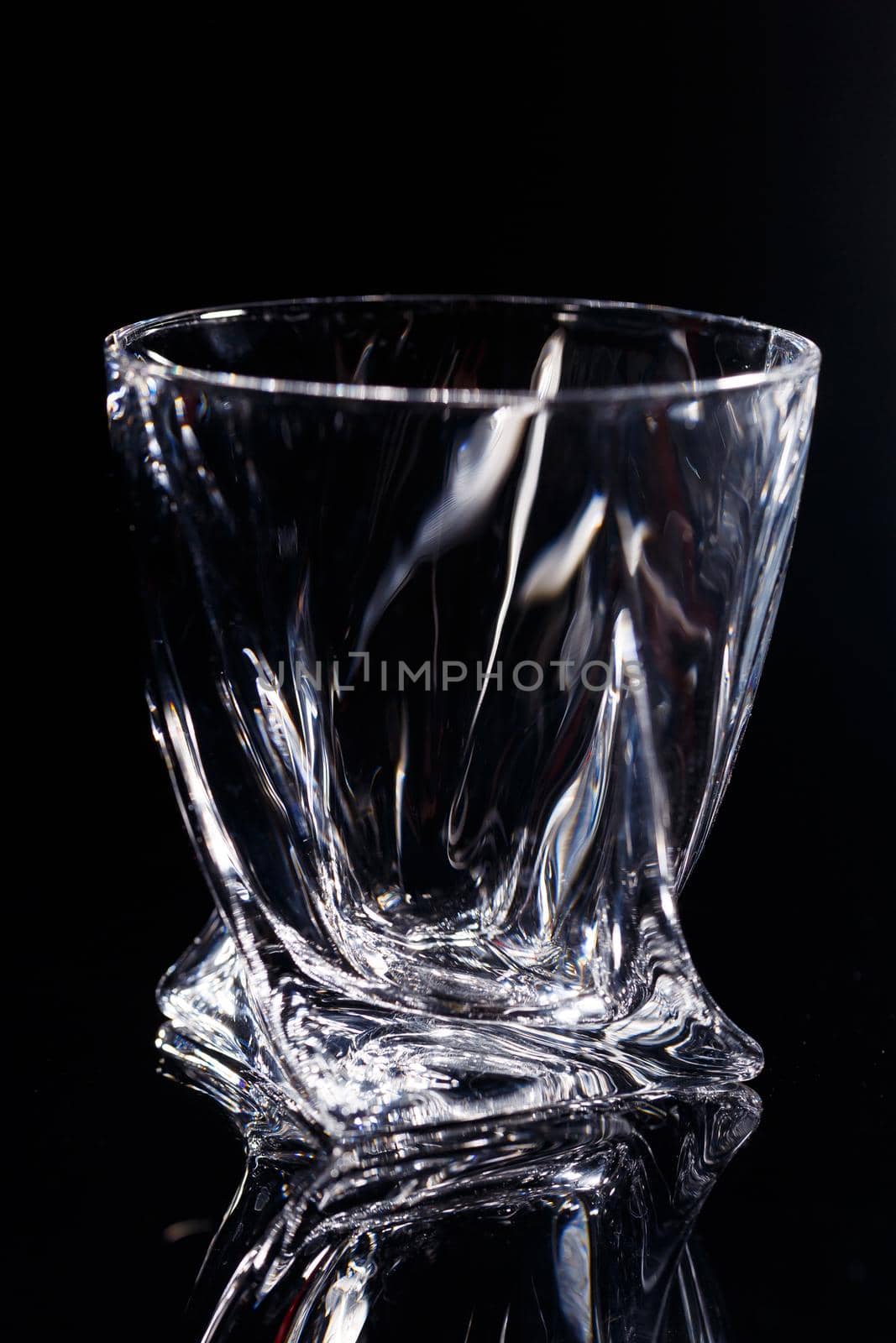 Black background stands a clean glass with reflection on a glass table. Facets on a Glass Cup by Dmitrytph