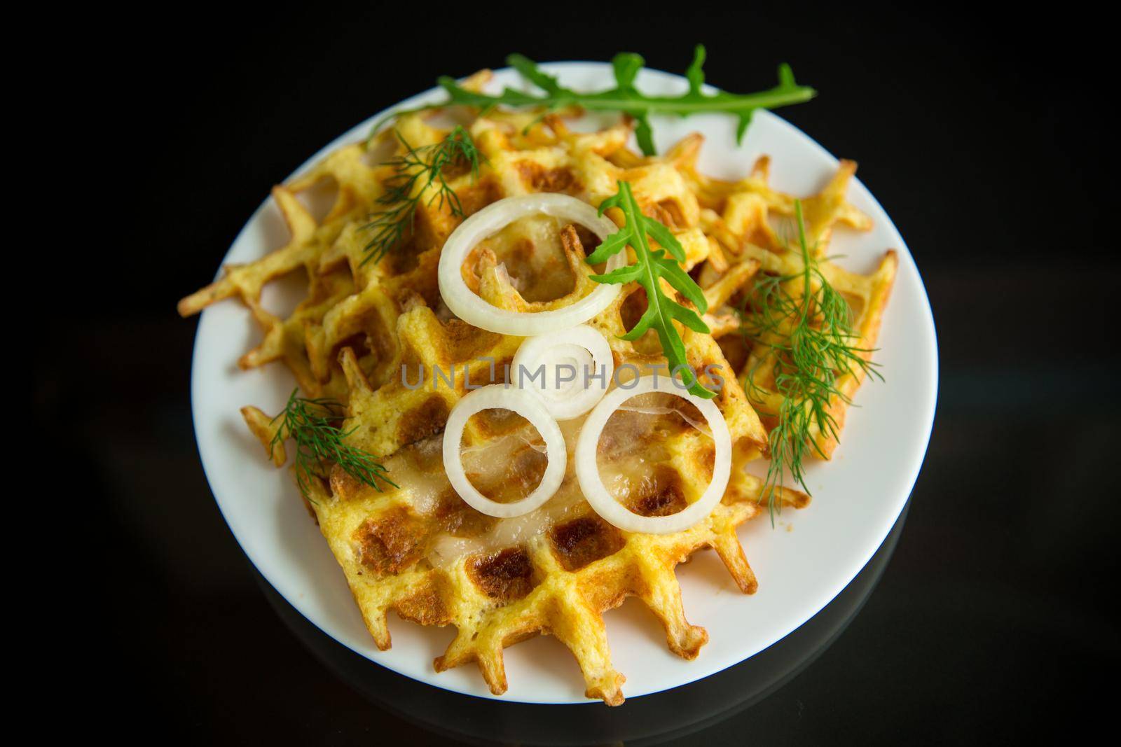 fried potato cheese vegetable waffles with bacon and onion in a plate isolated on black background.
