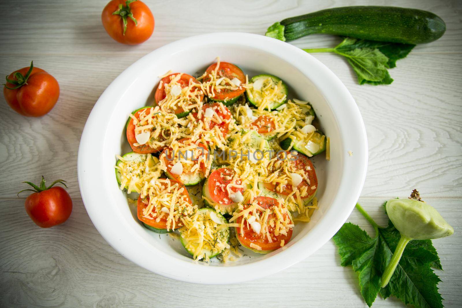 raw zucchini and tomatoes sliced with cheese, prepared for baking in a ceramic dish.