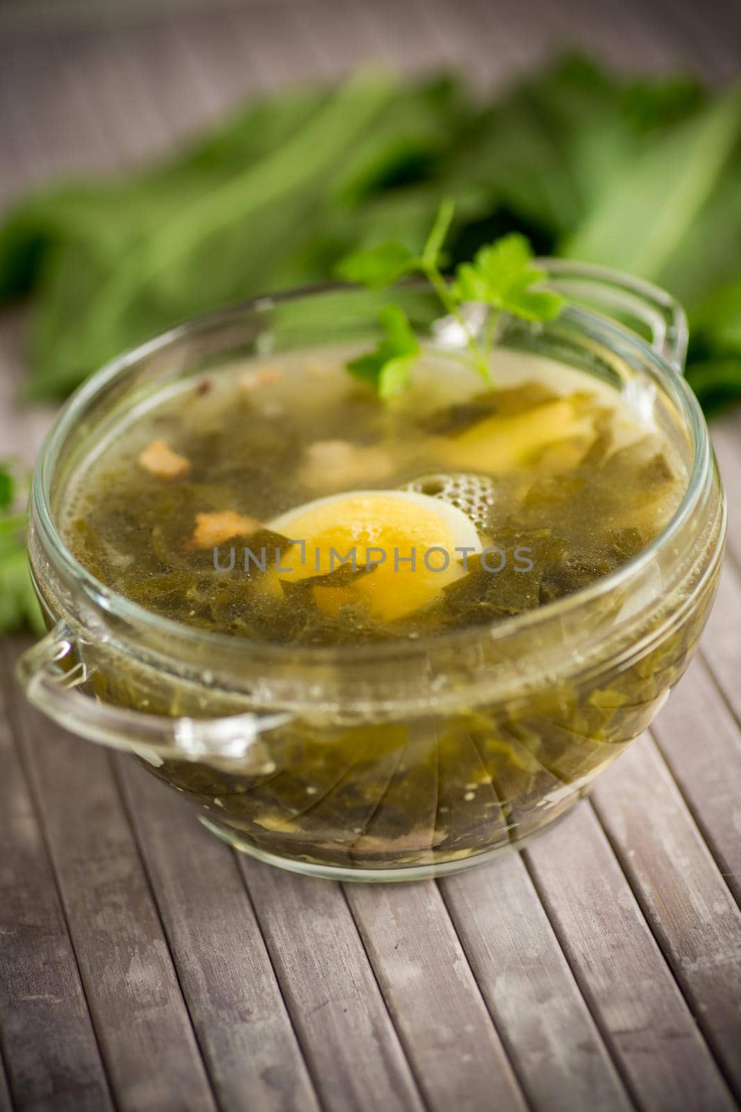 Spring soup from fresh sorrel with boiled eggs in a plate on a wooden table