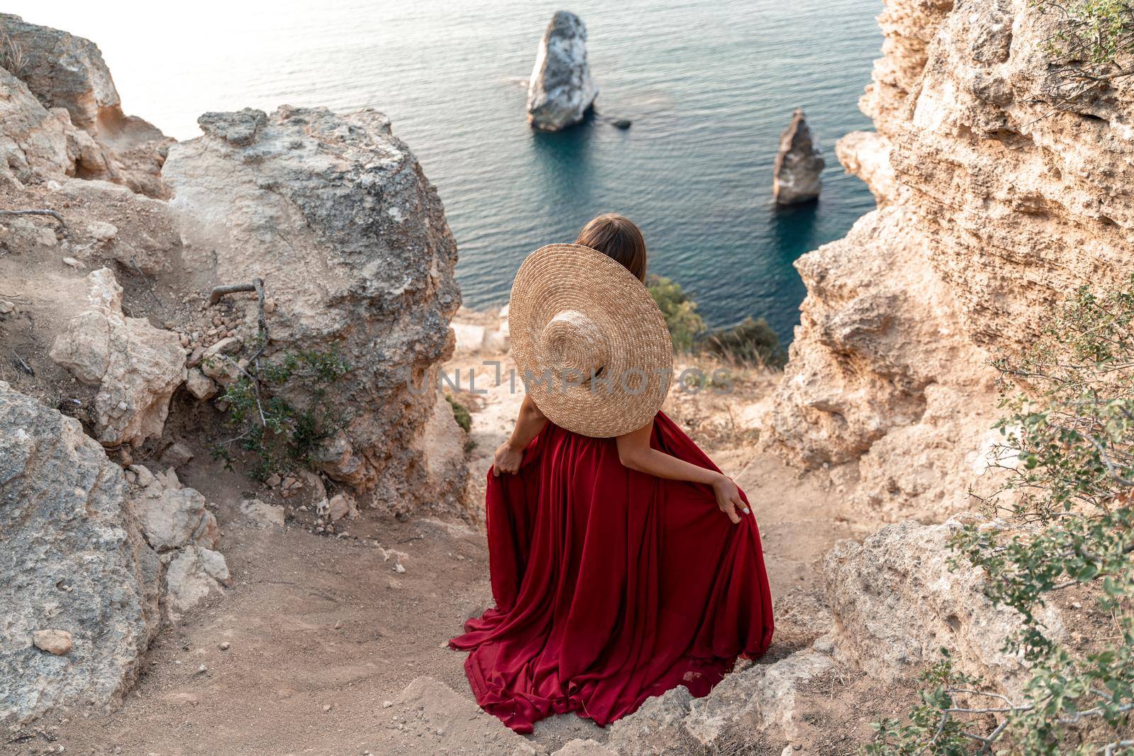 A girl with loose hair in a red dress sits on a rock rock above the sea. In the background, the sea. The concept of travel