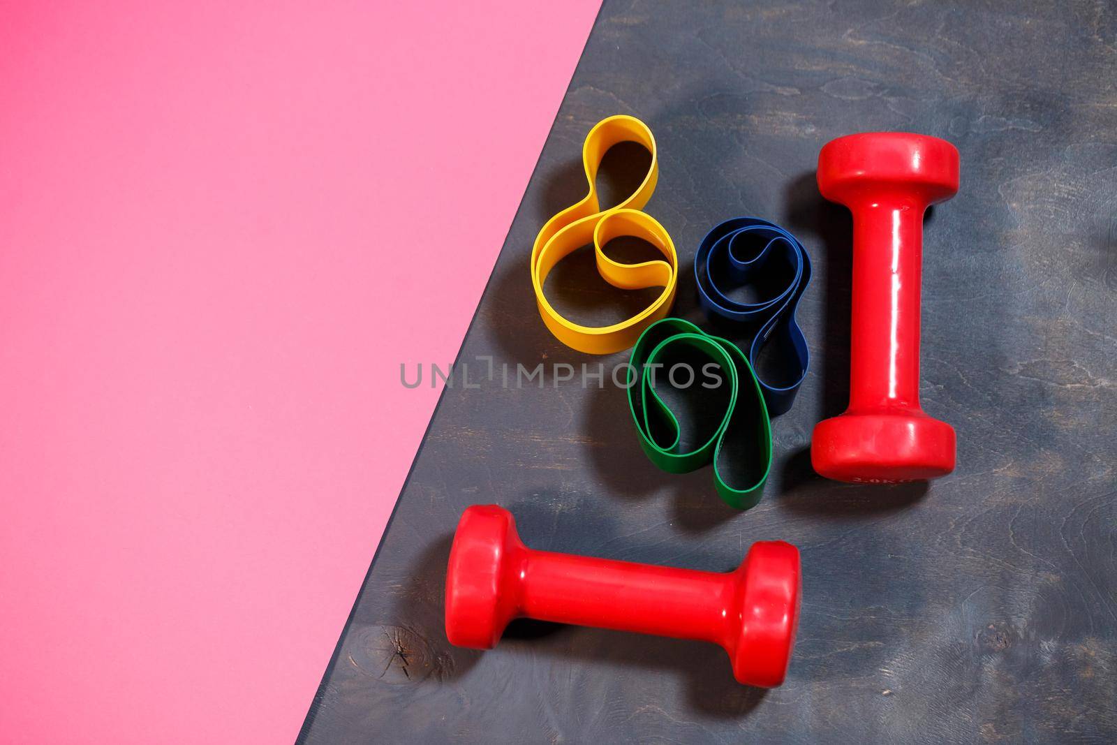 Red dumbbells and elastic bands for sports on a pink background. Healthy lifestyle. Fitness equipment for weight training. Muscle development and fitness training