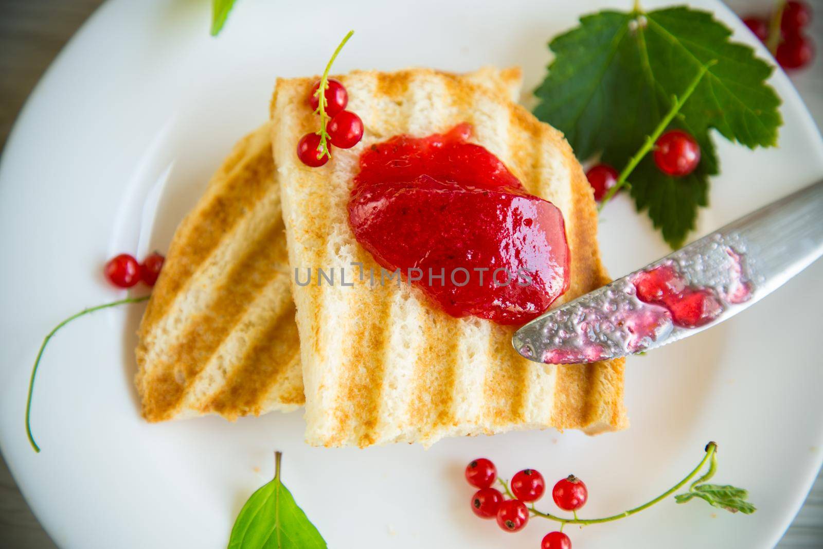 fried bread croutons for breakfast with redcurrant jam in a plate with berries on a wooden table.