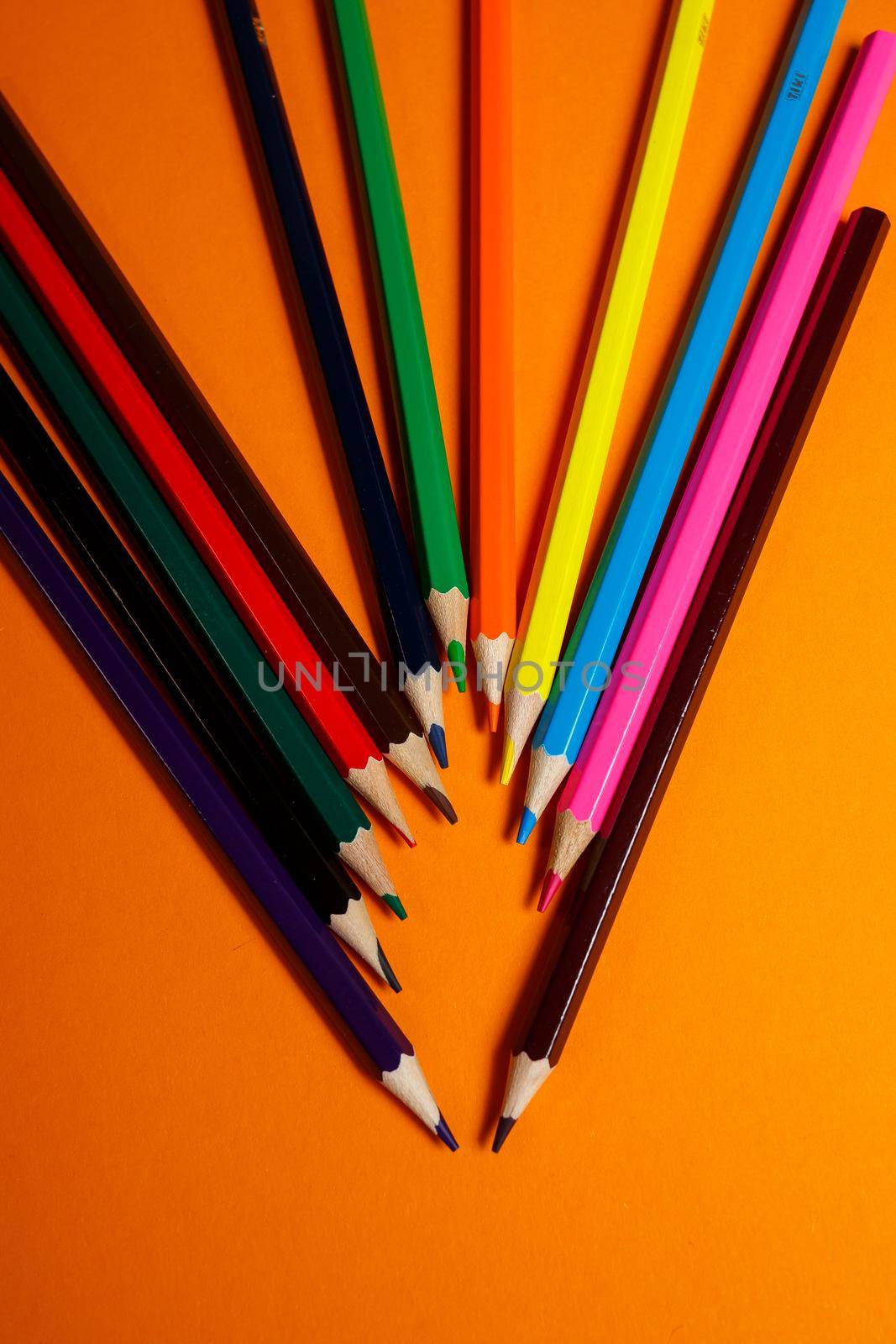 multicolored pencils for drawing stacked on an orange background. Stationery items