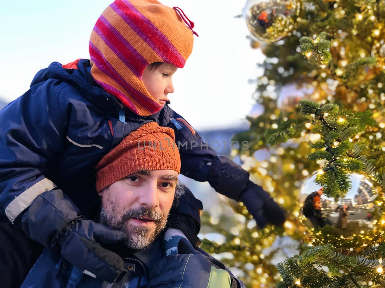 Father and son wearing winter hats spend time together at the Christmas tree
