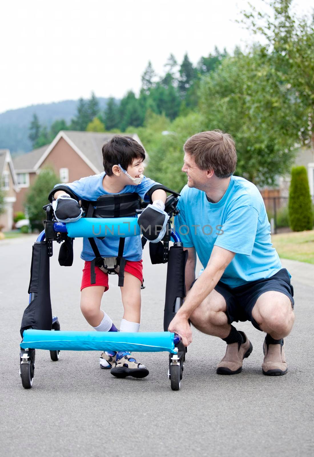 Father kneeling next to disabled son standing in walker