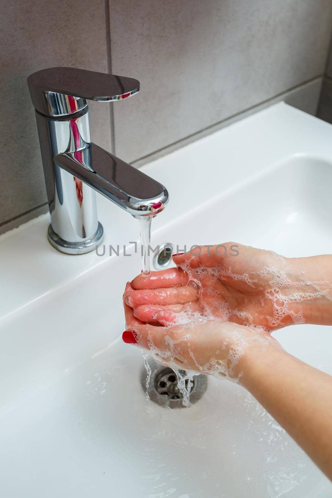 White sink with a silver faucet in the bathroom. Gray can with liquid soap for hands. Turning on the tap water, personal hand hygiene. Hand washing under running water