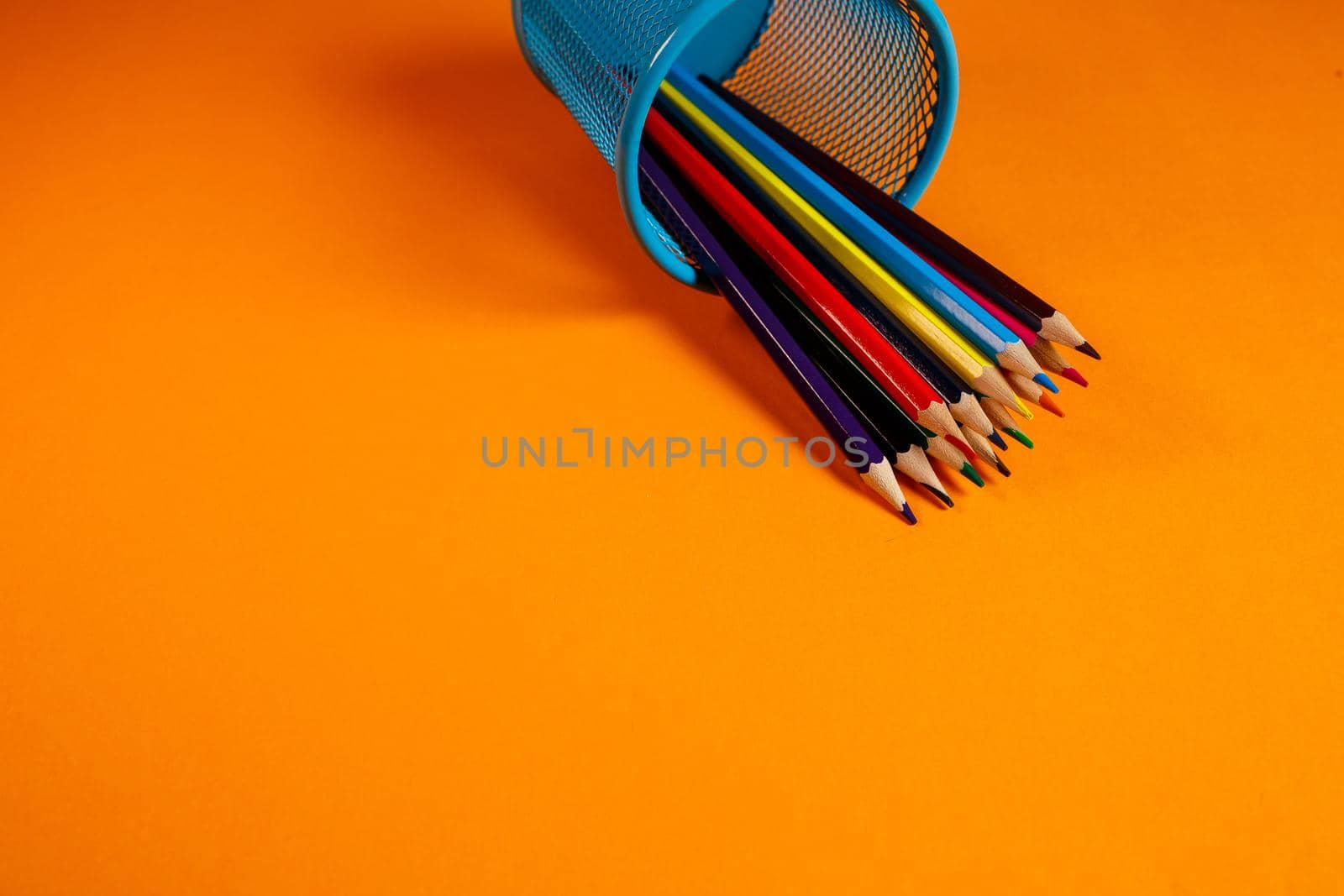 blue metal bucket with colored pencils for office on an orange background