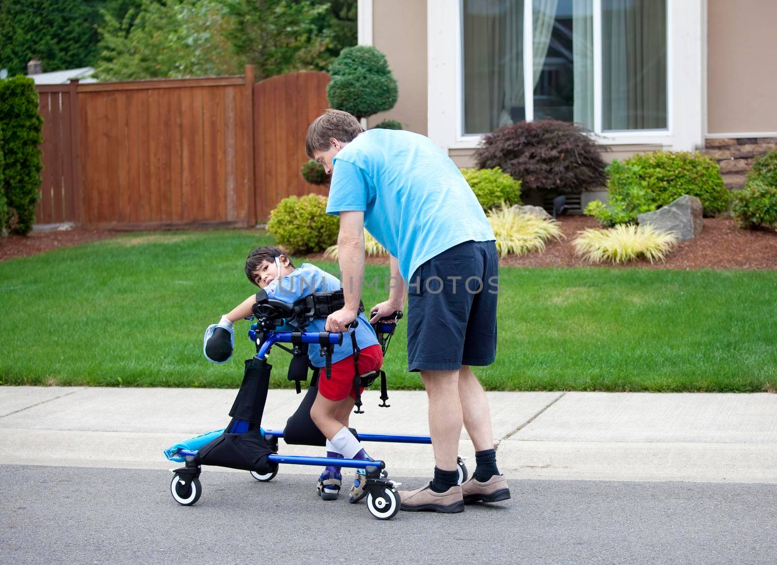 Father helping disabled son walk in his walker outdoors on road