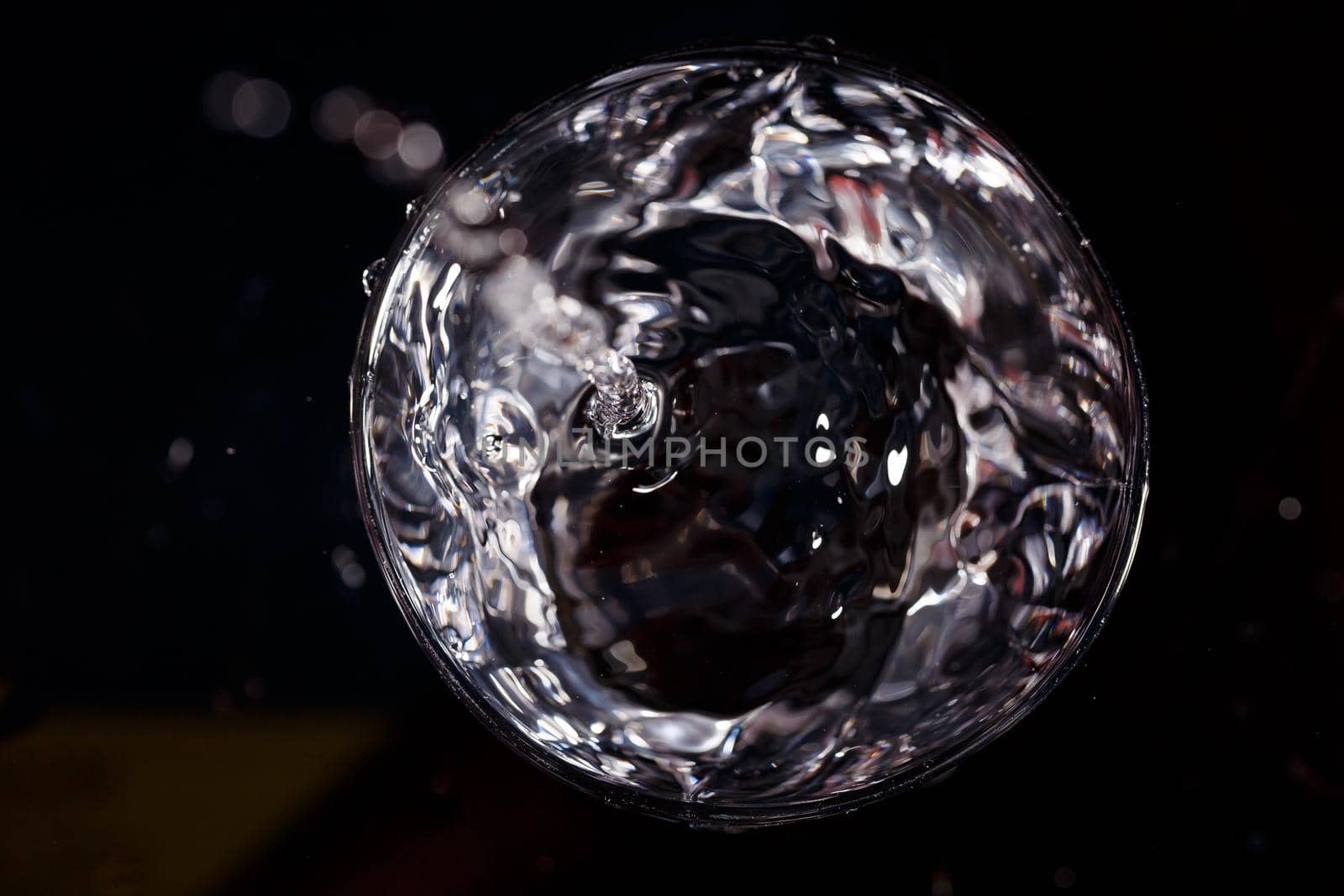 Black background is a glass in which a drop of water falls. Splashing water on glass