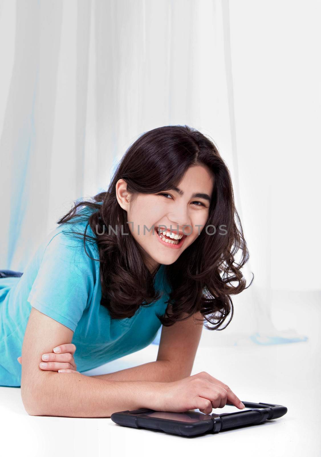 Biracial teen girl playing with tablet computer on the floor.