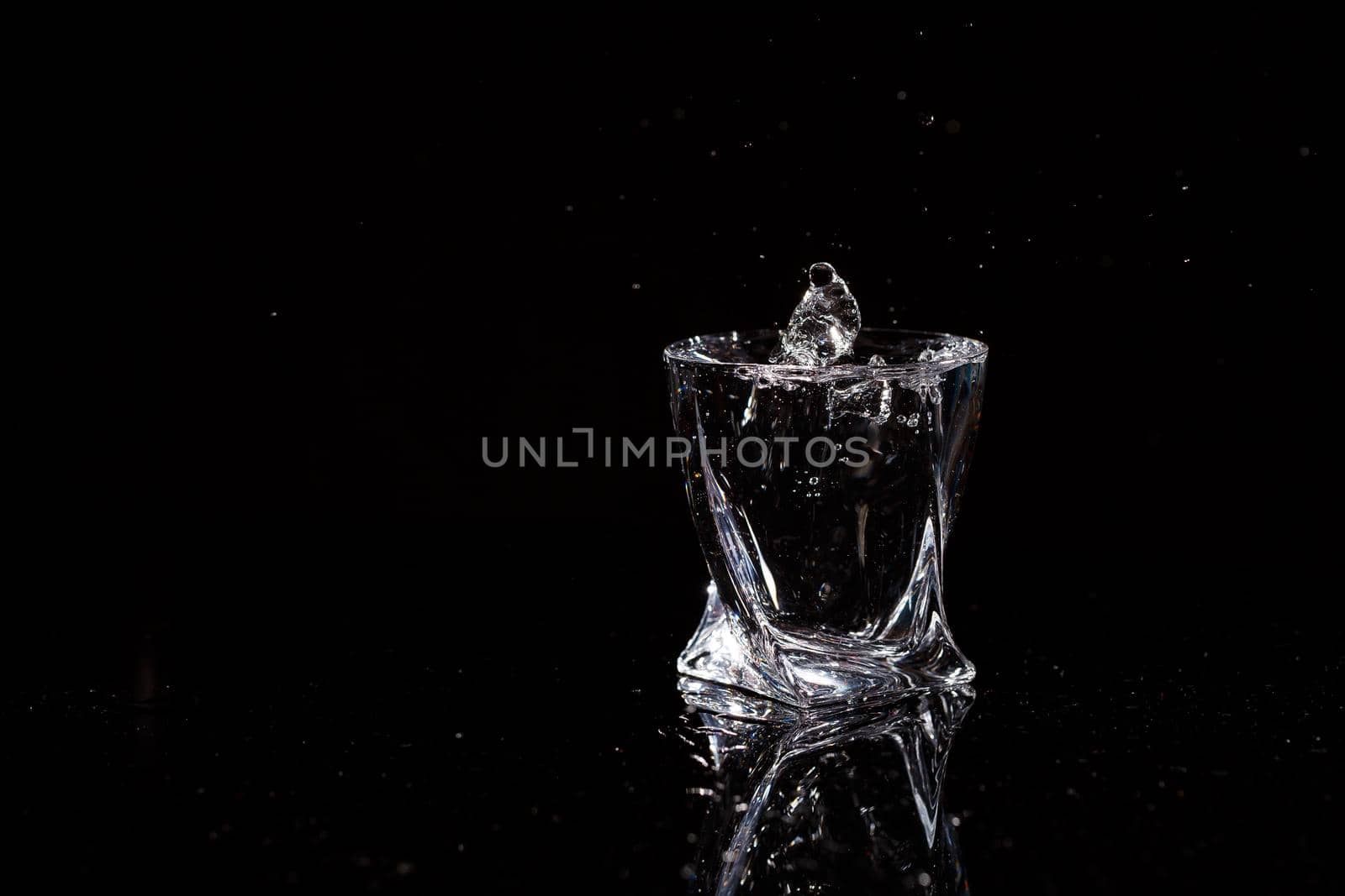 Black background is a glass in which a drop of water falls. Splashing water on glass