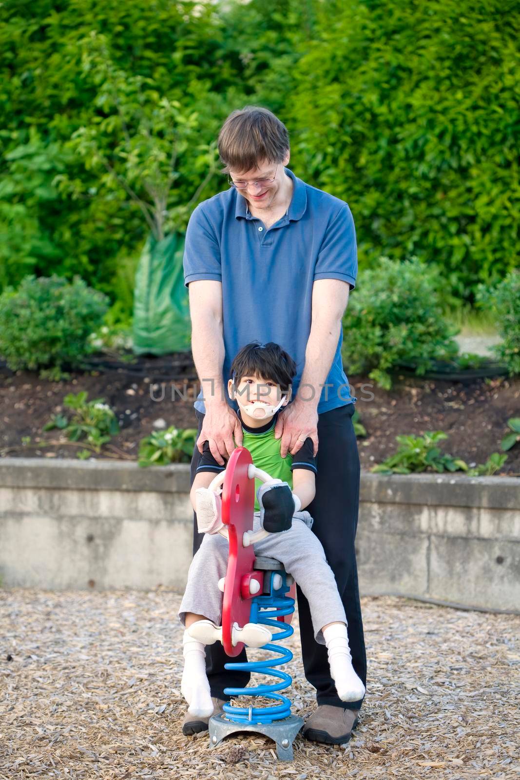 Father helping disabled son play on playground equipment