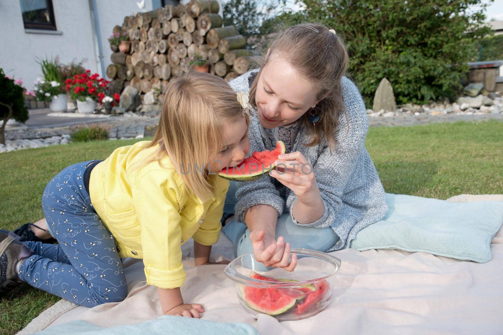 young mother feeds her daughter sweet watermelon, picnic in nature near the house.High quality photo