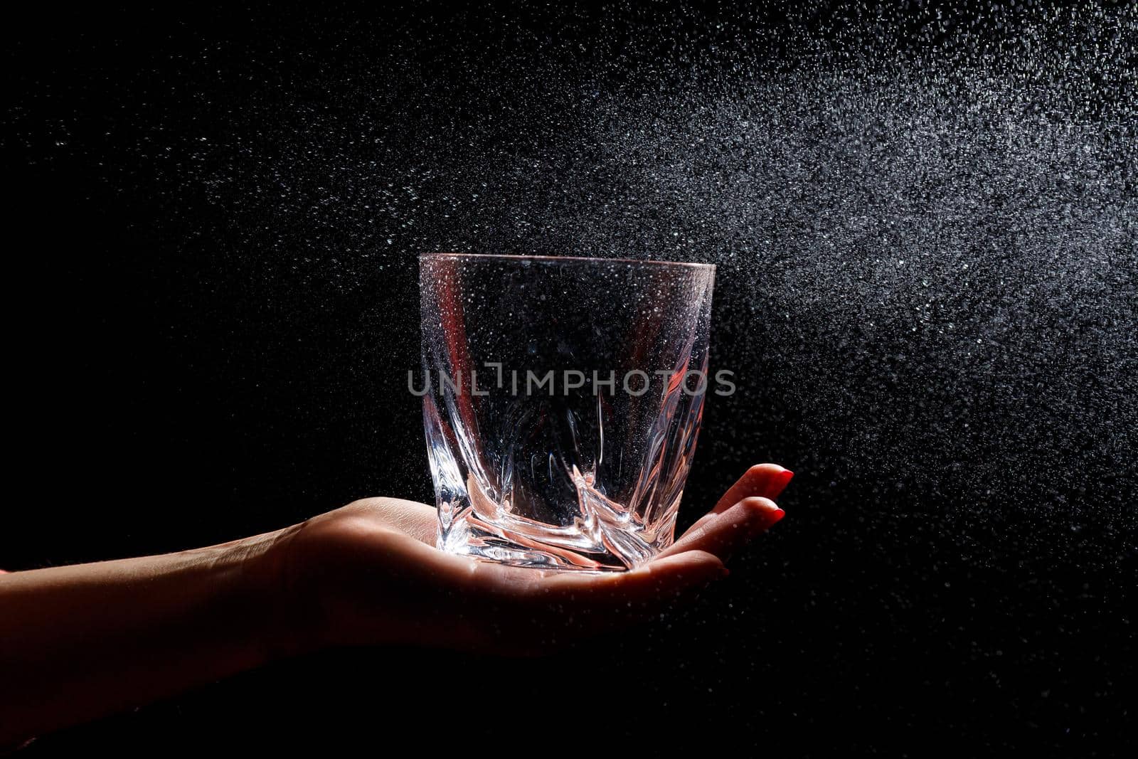Black background on it is a close-up of a clean glass in a hand. Spray on a glass of water. Insulated glass