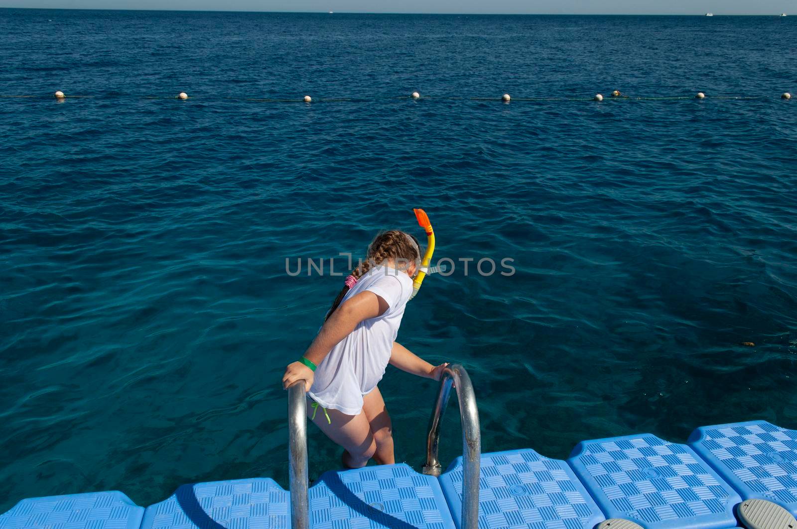 a little girl in a white t-shirt and a swimming mask, dives and swims in the salty Red Sea in Egypt, refreshes on a hot day, summer vacation adventure, summer vacation adventure. High quality photo