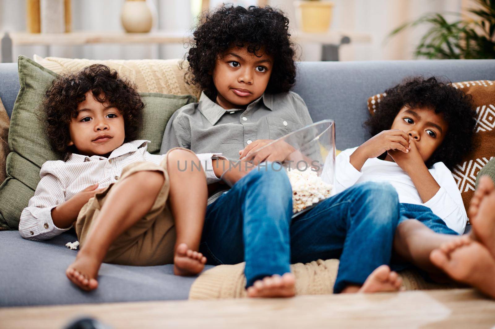 Cartoon time. Full length shot of three adorable little boys eating popcorn and watching tv together at home. by YuriArcurs