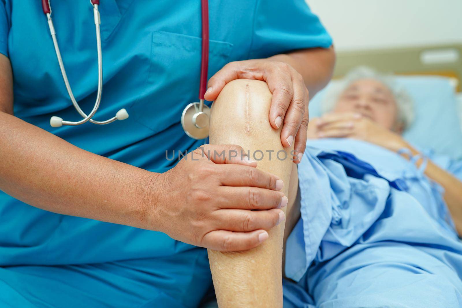 Doctor checking Asian elderly woman patient with scar knee replacement surgery in hospital.