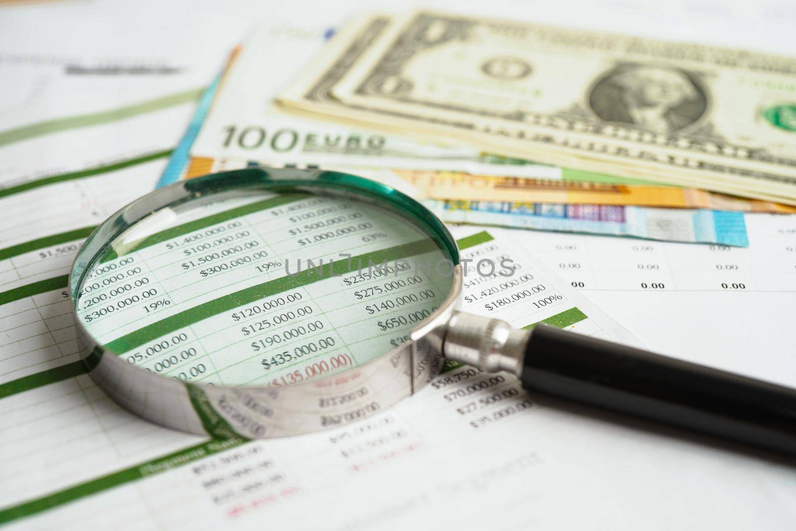 Magnifying glass on US dollar and EURO banknotes and graph, finance business trade concept.