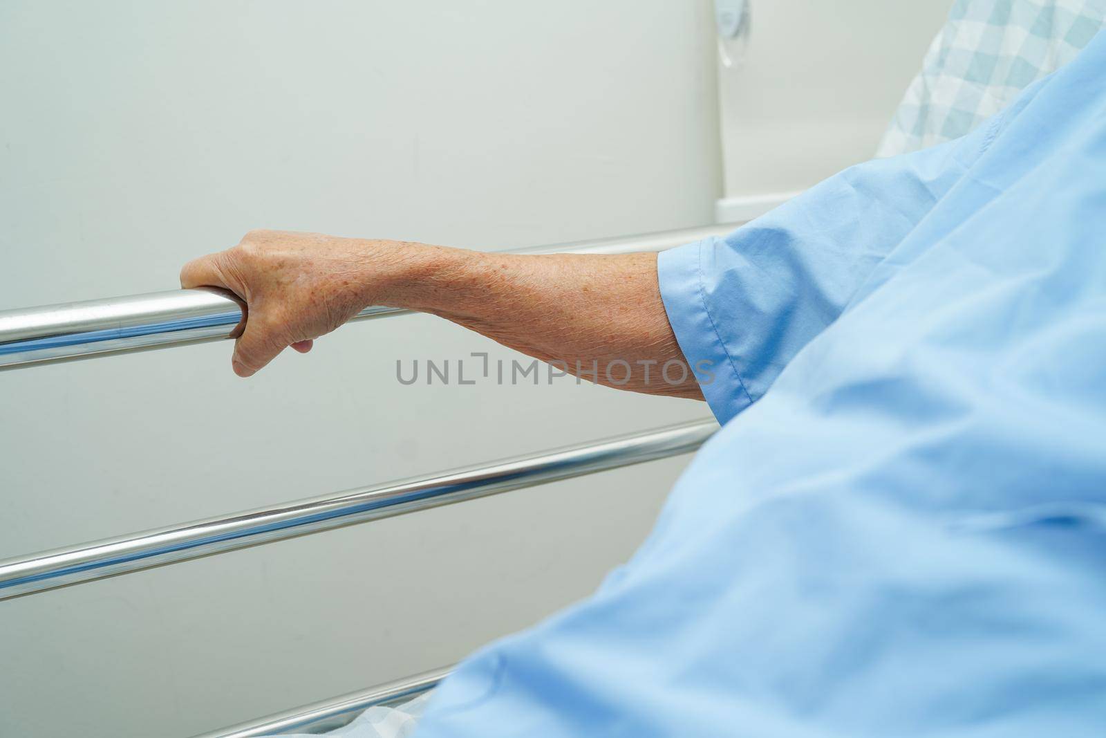 Asian elder senior woman patient holding bed rail while lie down with hope waiting her family in hospital.