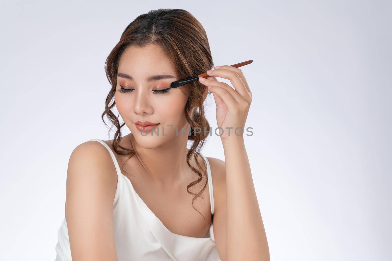 Gorgeous young woman putting black mascara on her long eyelashes with brush. Beauty cosmetic concept. Female model with perfect skin.