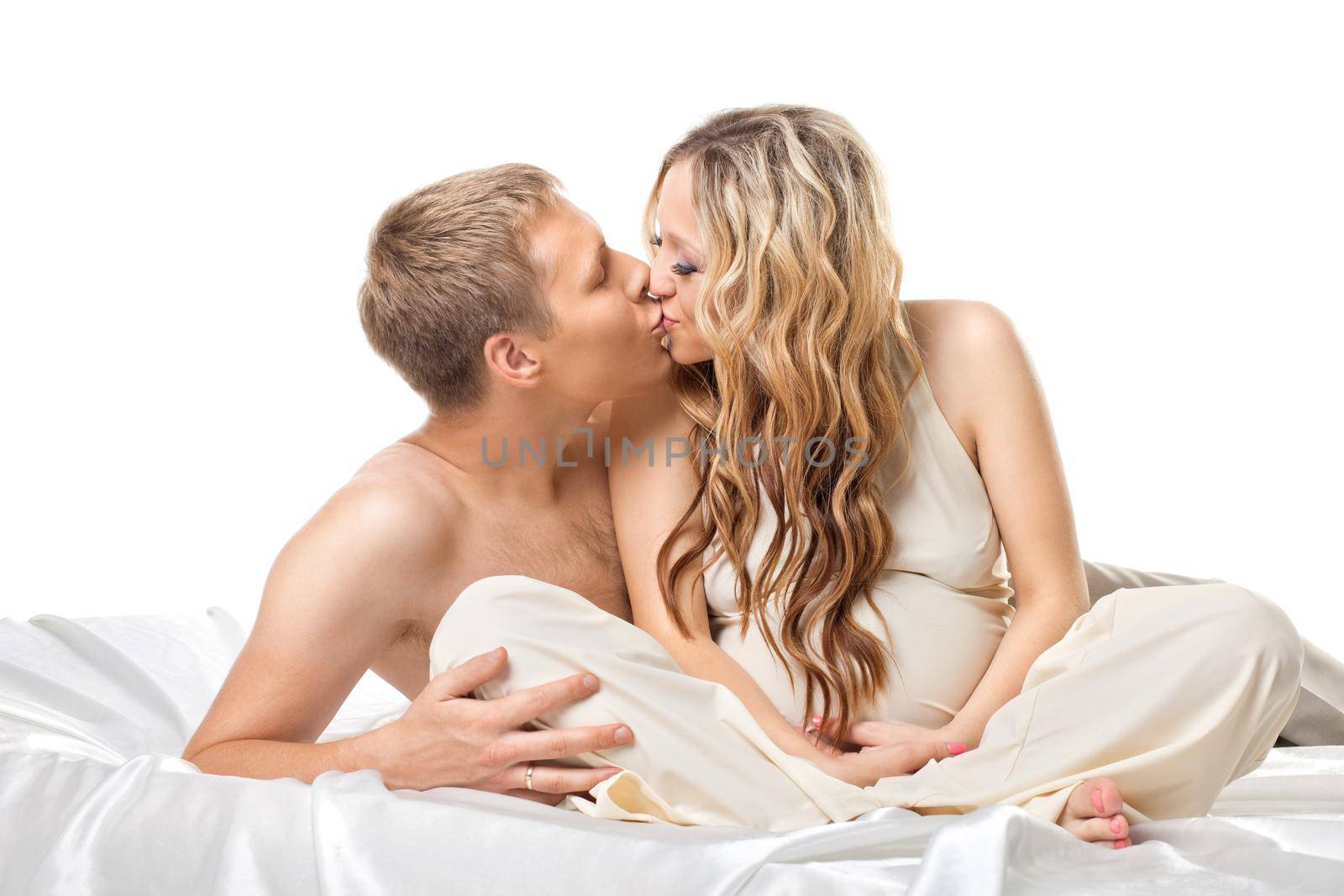 Young happy couple with pregnant woman in bed kiss together