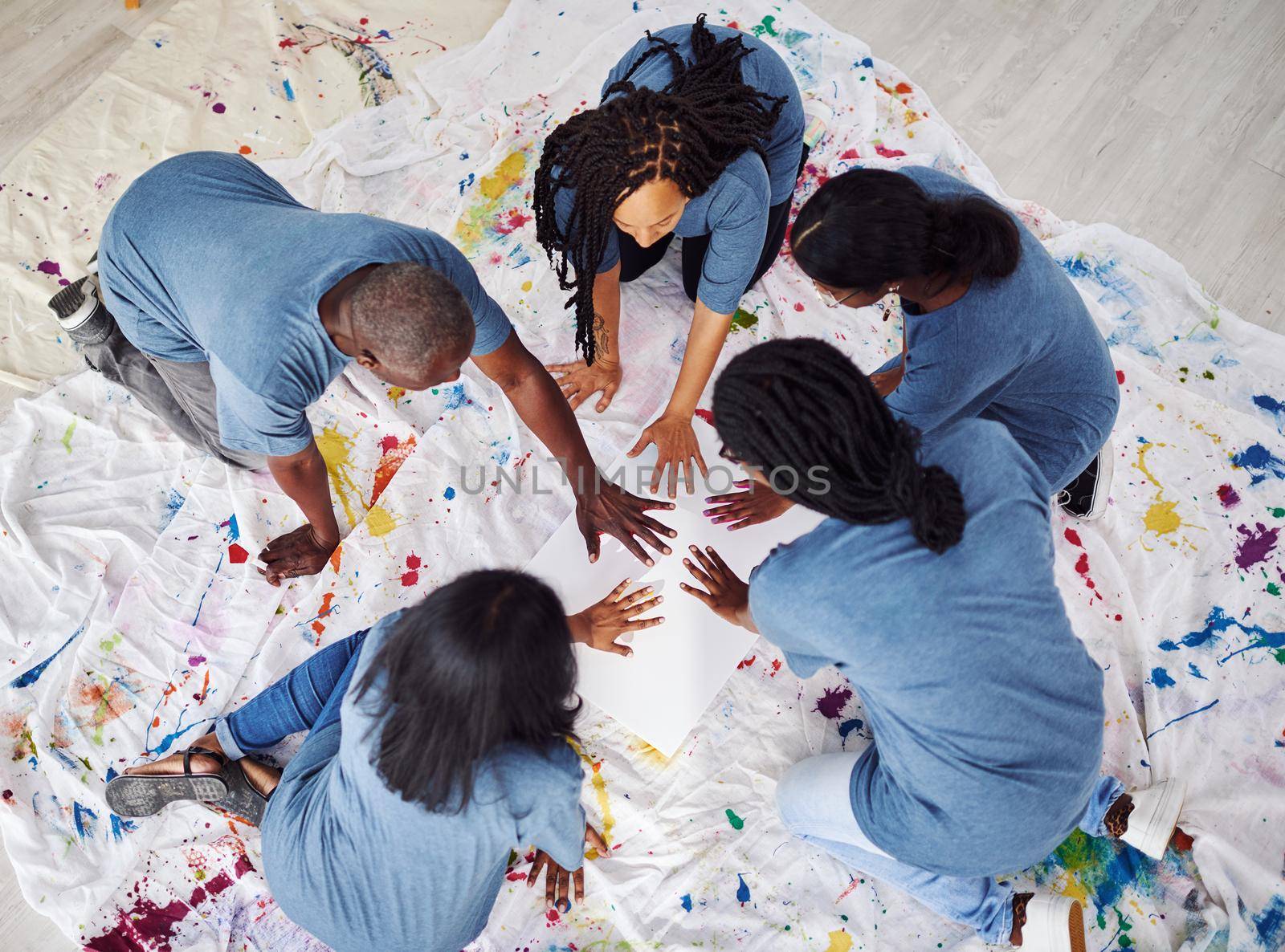 Get closer through creativity. a group of people of people leaving painted handprints on a white poster. by YuriArcurs