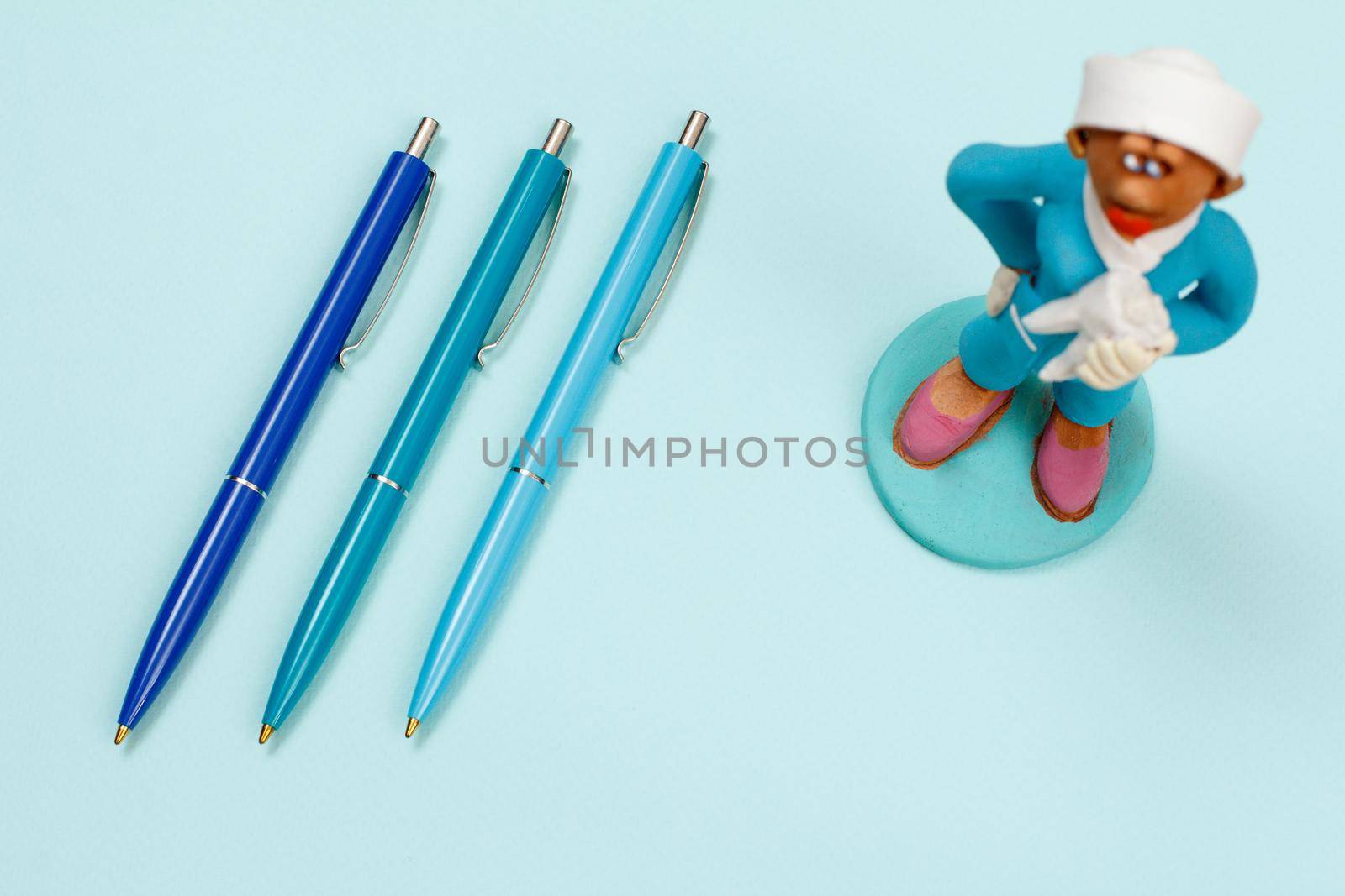 Three pens and plaster figure of a dentist on a blue background. Top view.