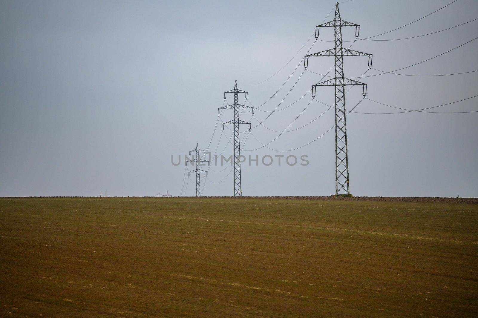 A high-voltage line runs over a bald field. The gray clouds of fog reinforce the wintry impression of the landscape.