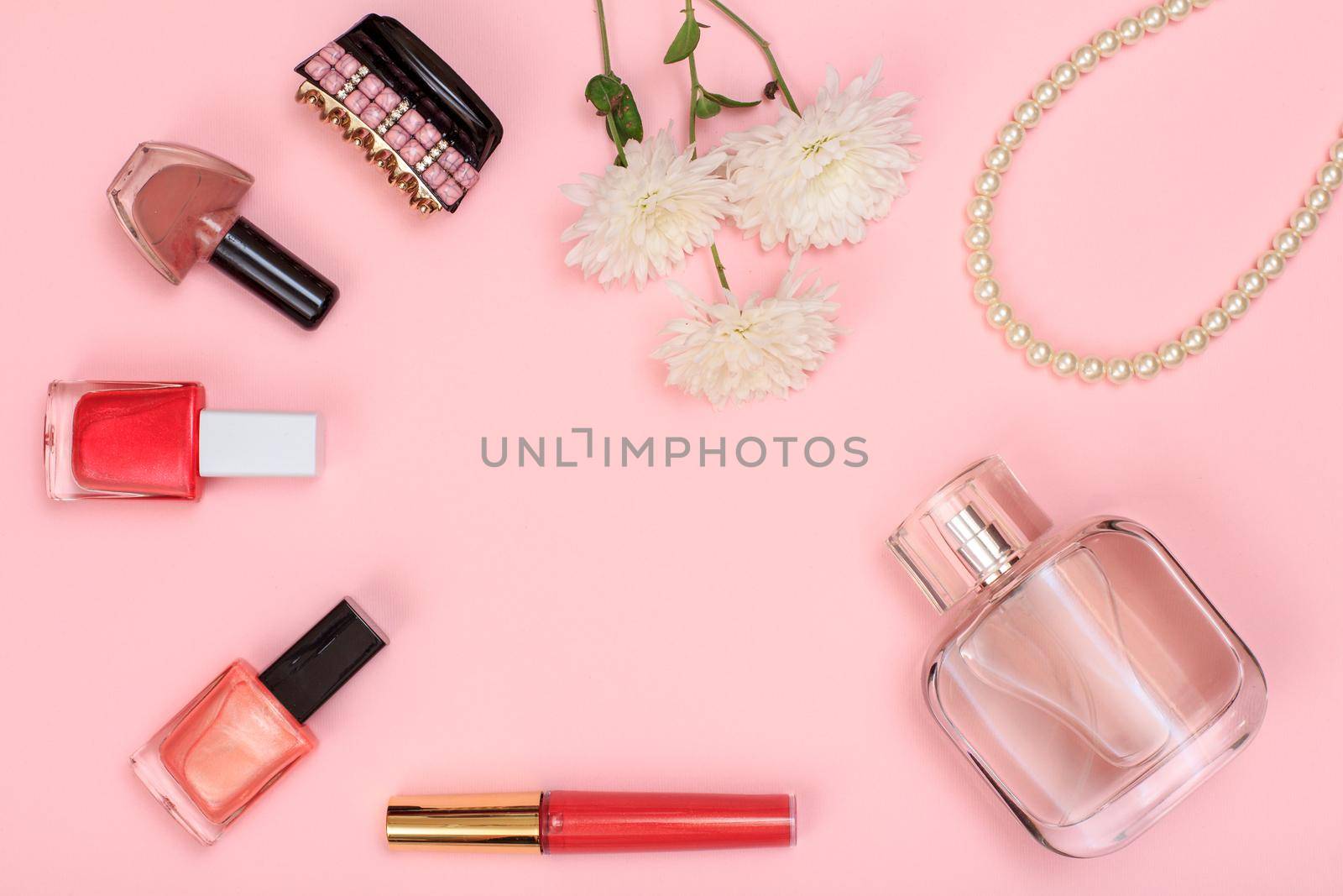 Lipstick, bottles with nail polish, hair clip, flowers, beads and bottle of perfume on a pink background. Women cosmetics and accessories. Top view.