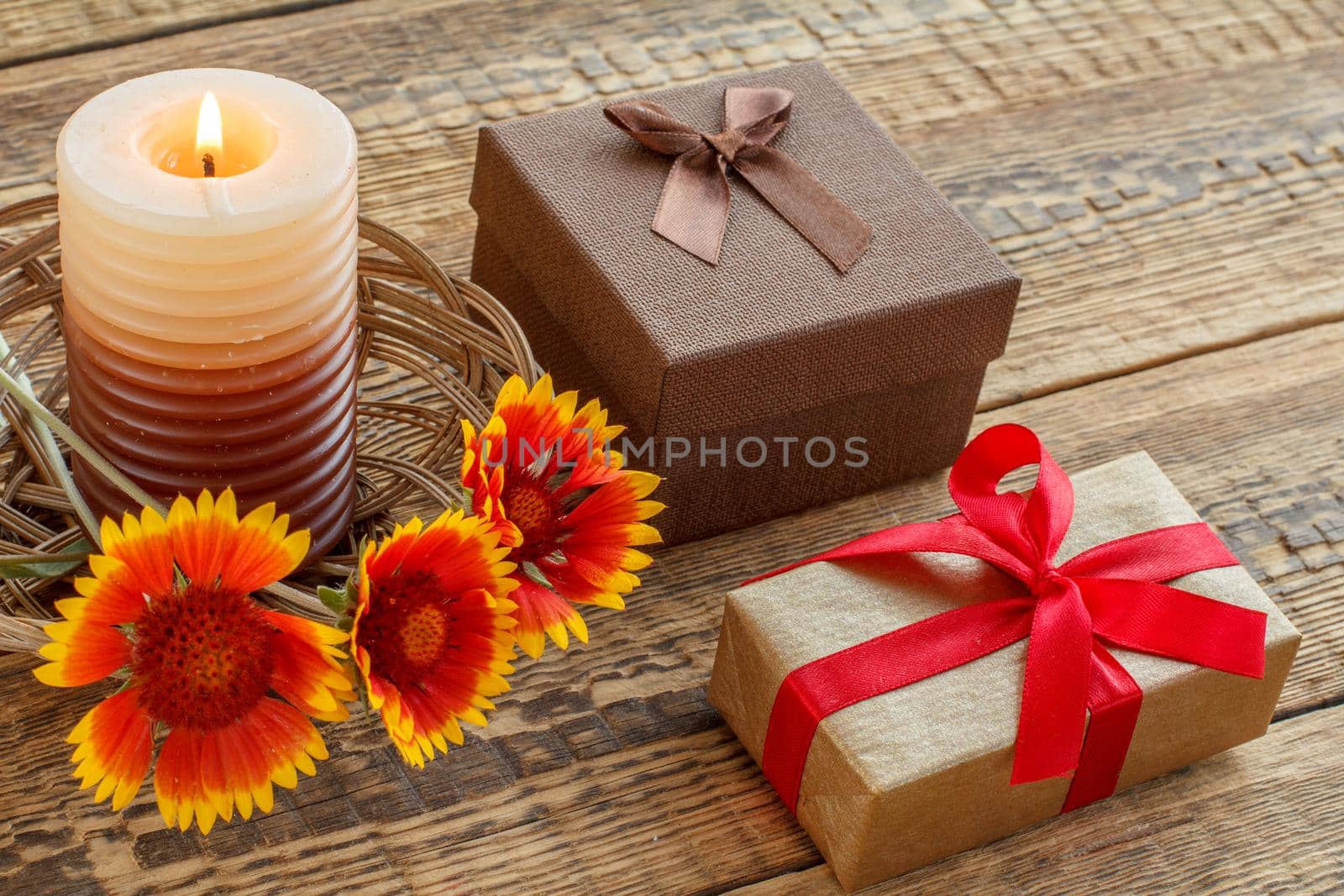 Burning candle, gift boxes and flowers on wooden boards. Top view. Holiday concept.