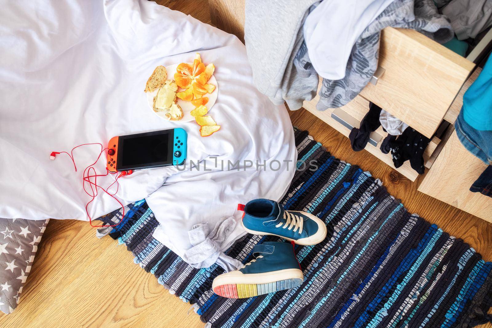 mess in the teenager's room in the morning, top view. Scattered clothes, a blanket, a set-top box with headphones, shoes and food on the floor. The concept of the difficult age of the child, education