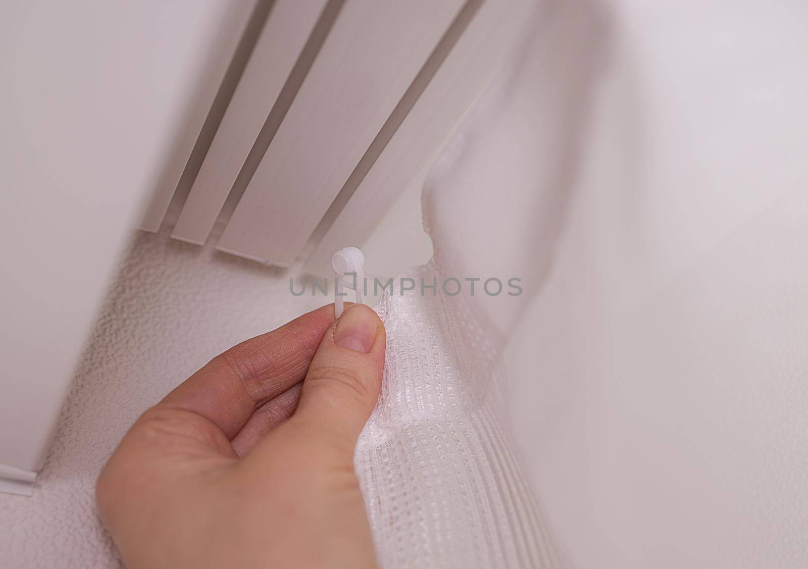 Close-up, the hands of a European woman dress a white curtain on the window. Home improvement concept, cozy, modern interior. Decorative design of the apartment with your own hands or a professional