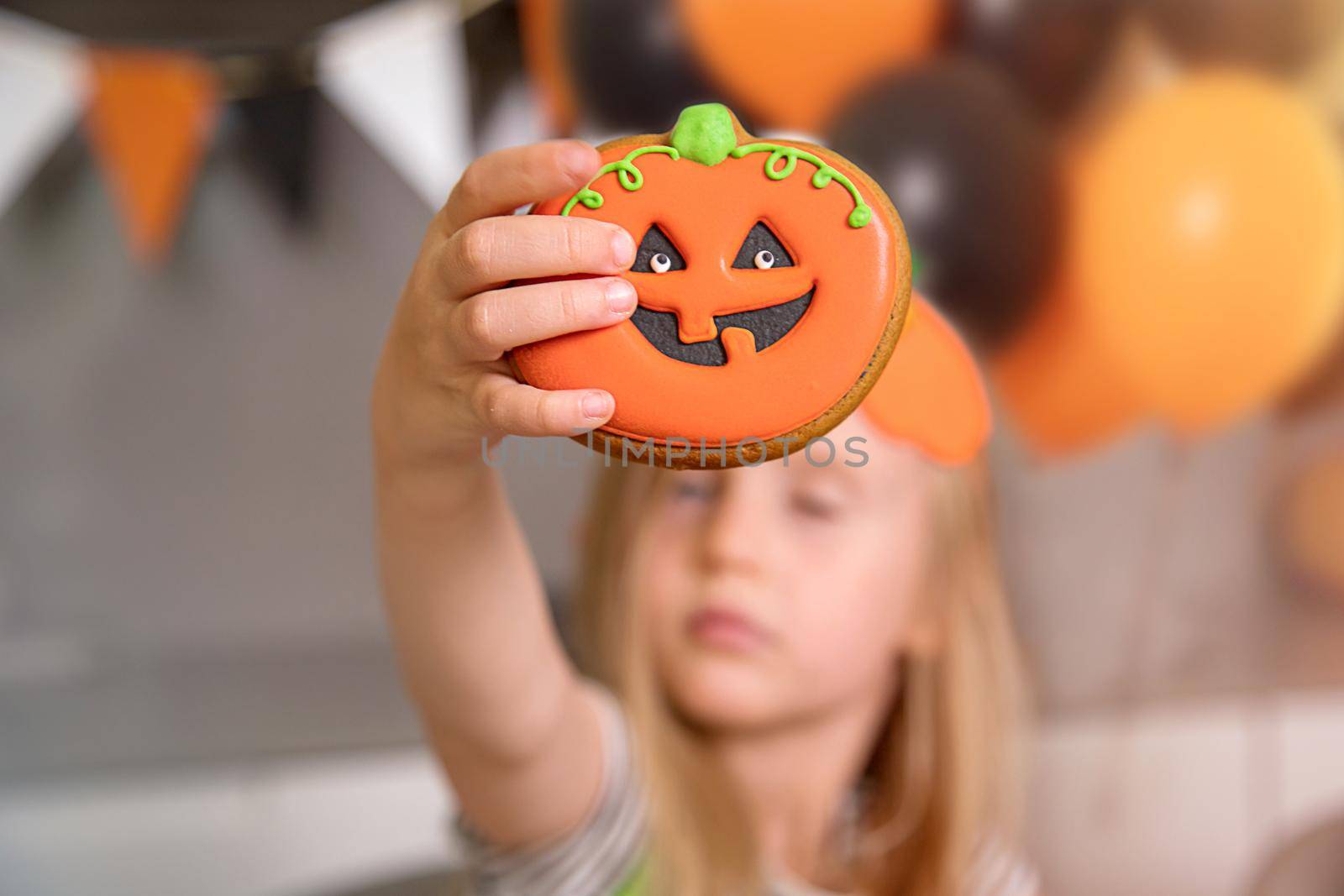 Happy Halloween holiday. A close-up of a girl shows a homemade gingerbread cookie, it is drawn like a pumpkin. the concept of homemade, holiday baking and unusual desserts to order.