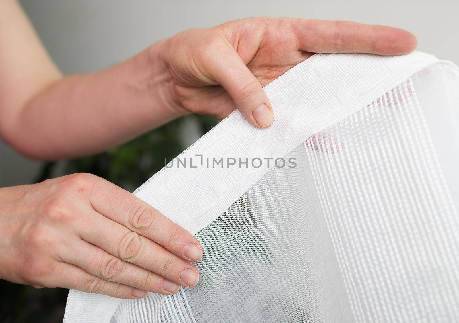 Close-up, the hands of a European woman demonstrate a piece of curtain, which is stitched with a special tape to hang the curtains. The concept of housekeeping, hobby, cozy home.