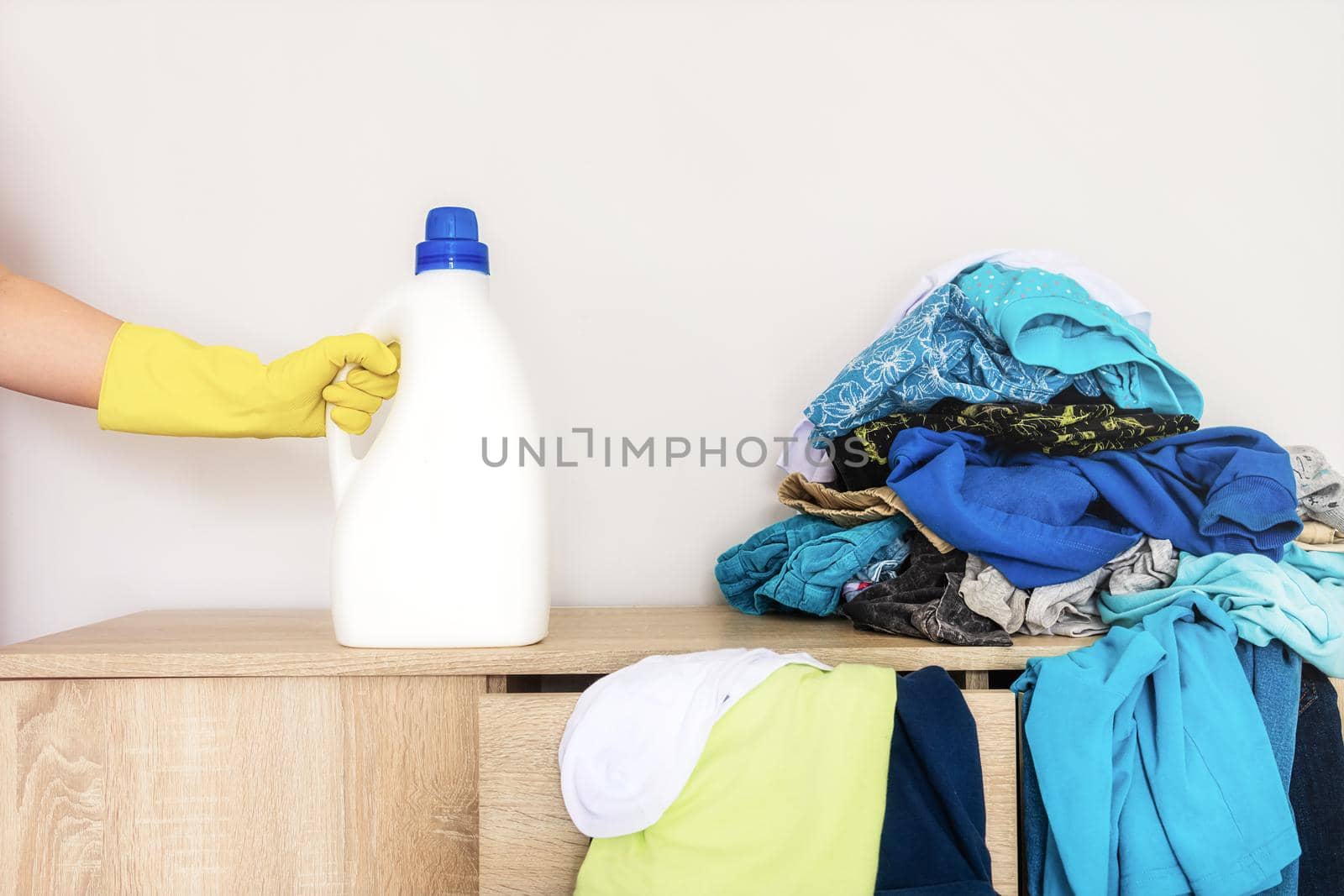 Close-up of a female hand in a yellow rubber glove holding a bottle of liquid laundry detergent. Label mockup, logo for cleaning, bleaching, house cleaning. mess, hygiene concept, space organization