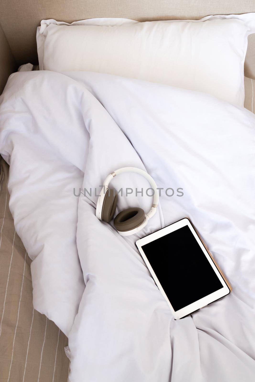 close-up, top view white bed on which lies a tablet and headphones. The concept of home learning, listening to music and entertainment at home. Audiobooks and computer games from the comfort of your bed.