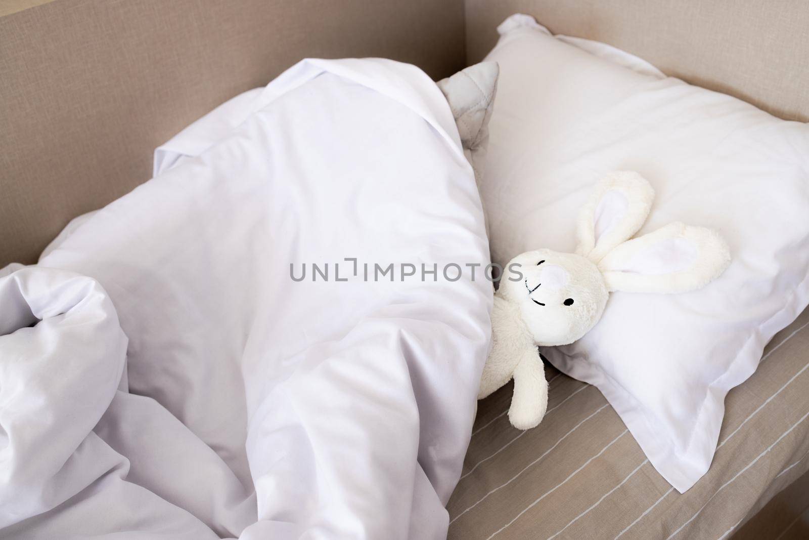 Close-up of a baby bed with white linens and copy space. mockup for textile, care concept, softness, cleaner and hygiene. A pillow, a blanket and a bunny lie on a brown white-striped sheet, top view.