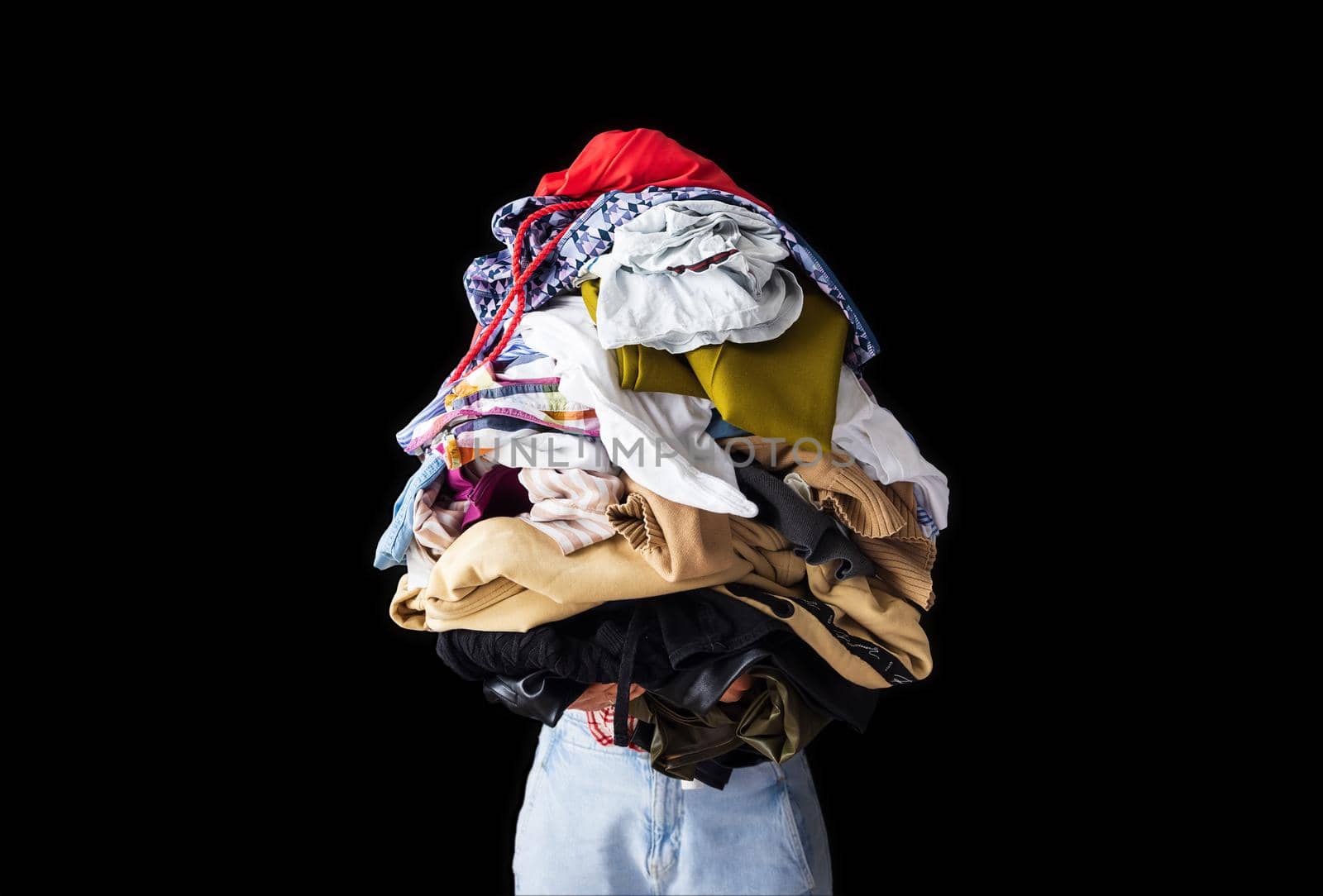 close-up, isolated object, a young woman holds in her hands a large pile of colored, crumpled clothes on a black background. The girl's head is not visible, copy-paste for your design