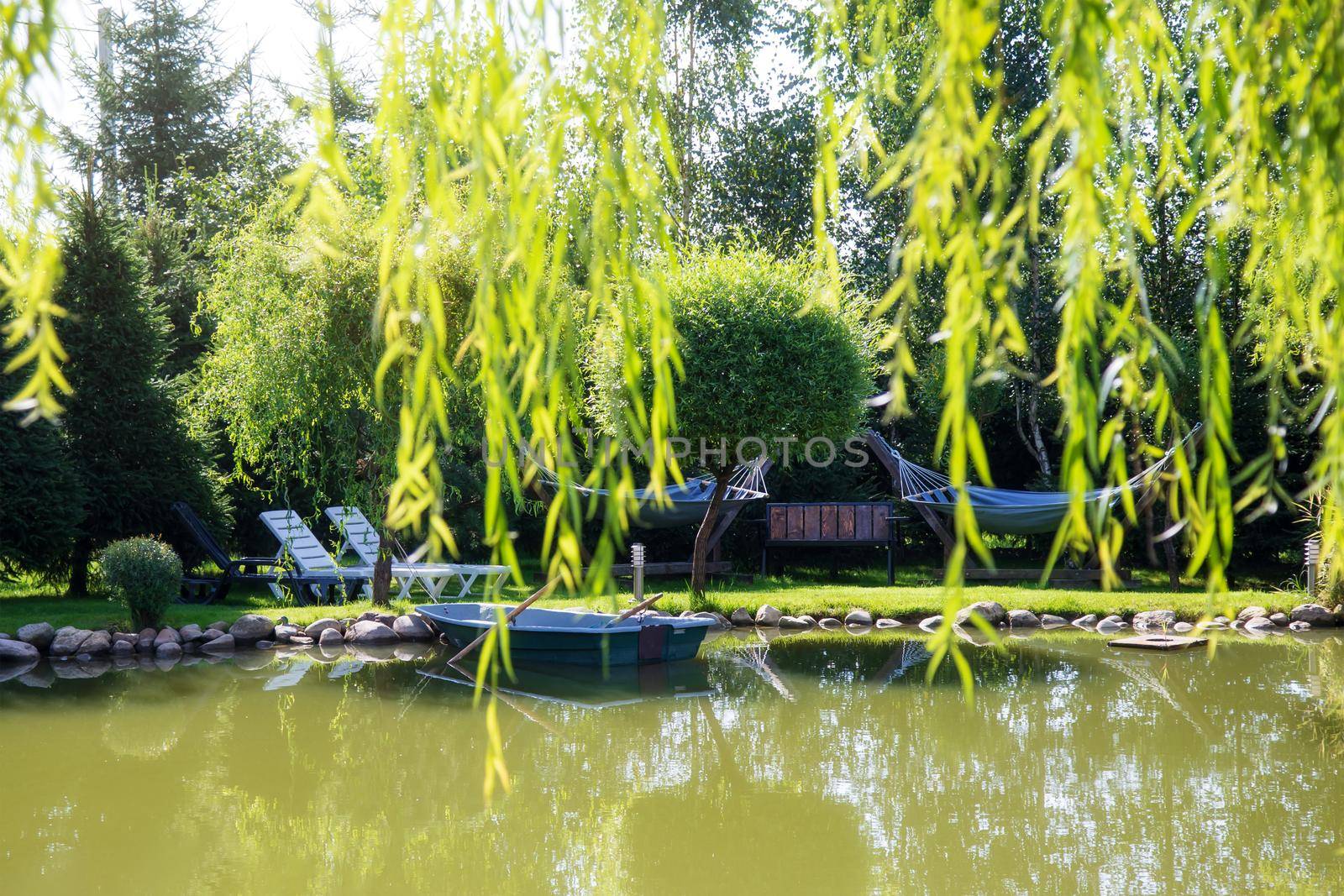 Rural landscape on a sunny summer day. A small lake with wooden boats and a place to relax surrounded by green trees. There are no people around. concept of tranquility meditation and balance