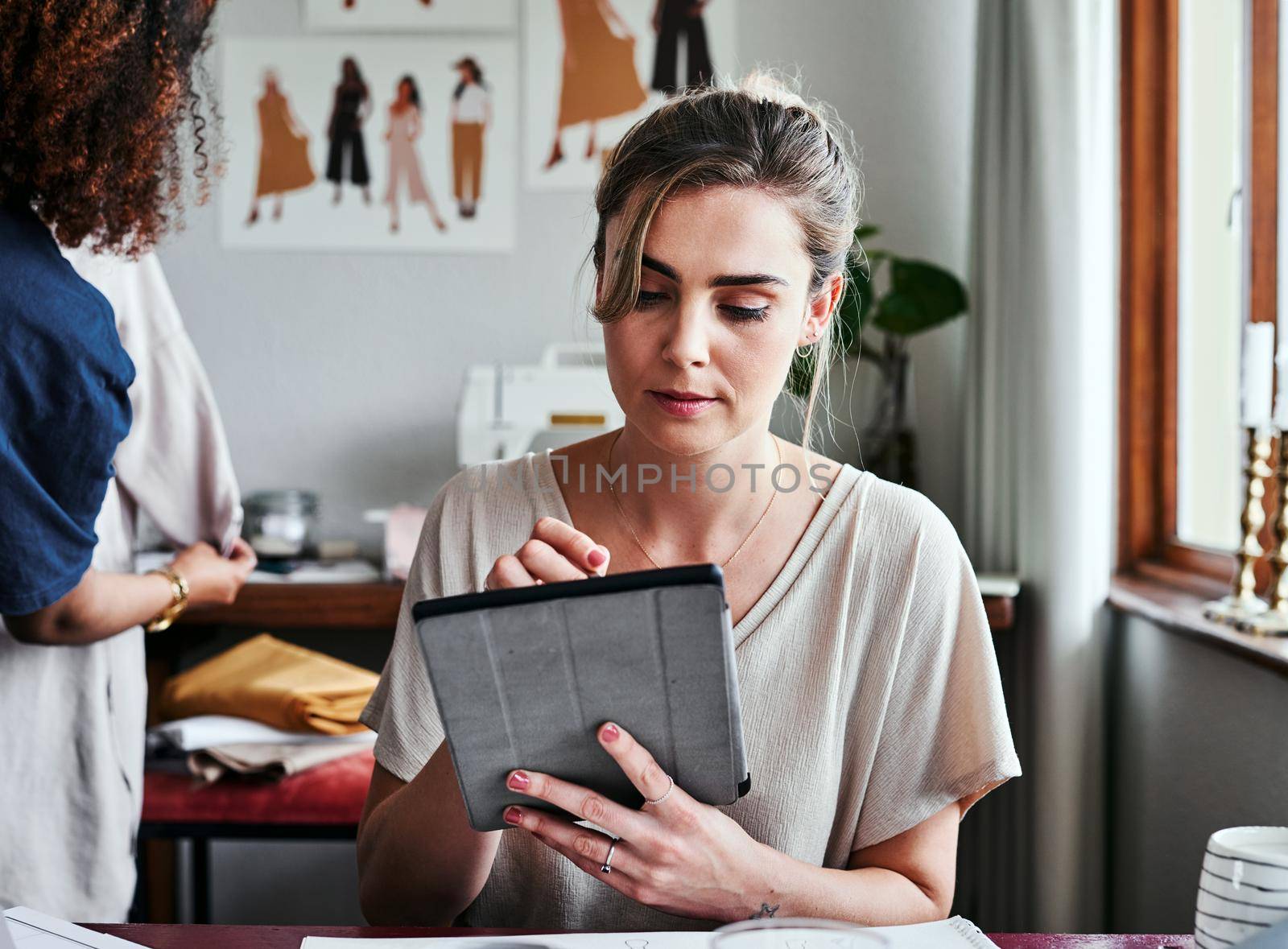 Studying a few fashion trends online. a fashion designer using a digital tablet while sitting in her workshop. by YuriArcurs
