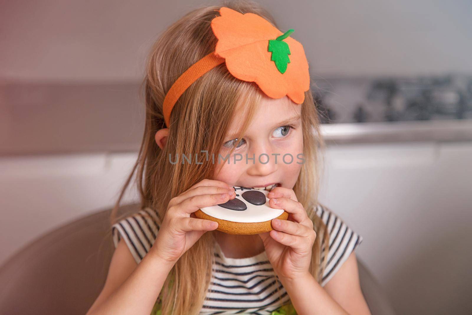Portrait of girl in pumpkin costume, she eats homemade cookies with painted face by Ramanouskaya