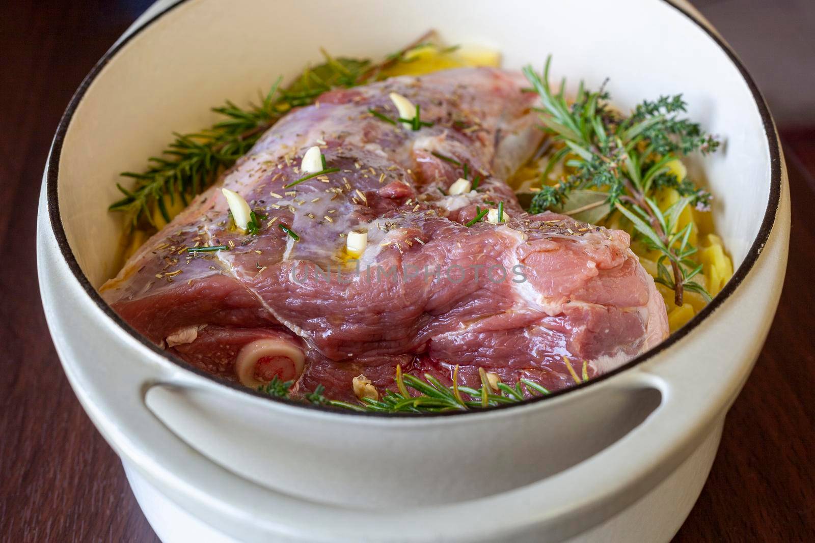 raw leg of lamb prepared to cook with sliced potatoes and provencal herbs, top view