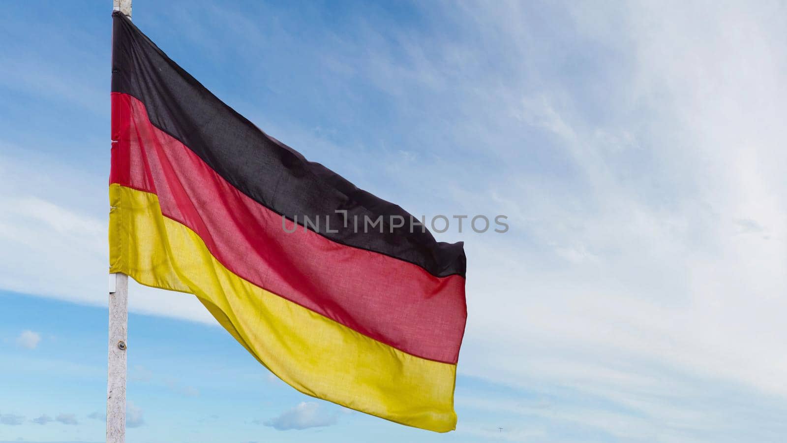 The official flag of Germany waving on a blue sky background. Horizontal banner design, with the German flag hanging on a sunny background with white clouds. Deutschland flag wide banner.