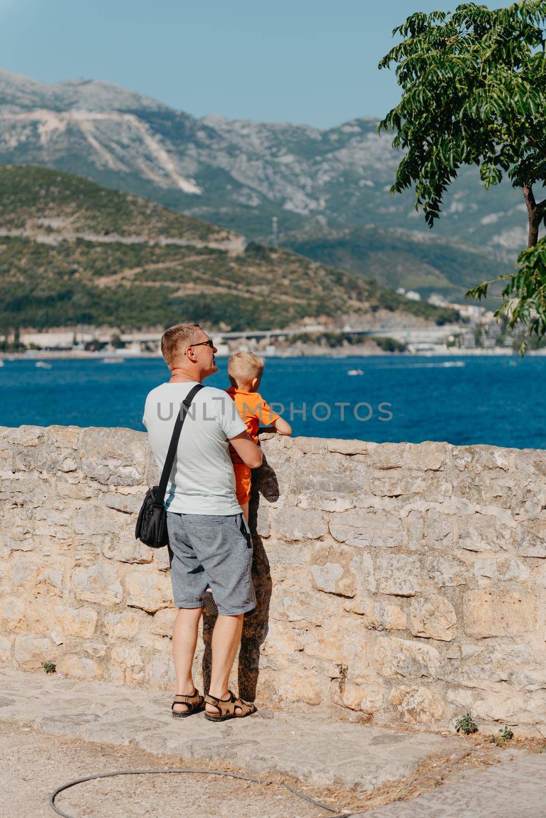 Cute family are having fun on the beach. Father and child against the background of the blue sea and sky. Travel, active lifestyle, vacation, rest concept. a man with a child on the shore. tourists on the shore of Budva, Montenegro by Andrii_Ko