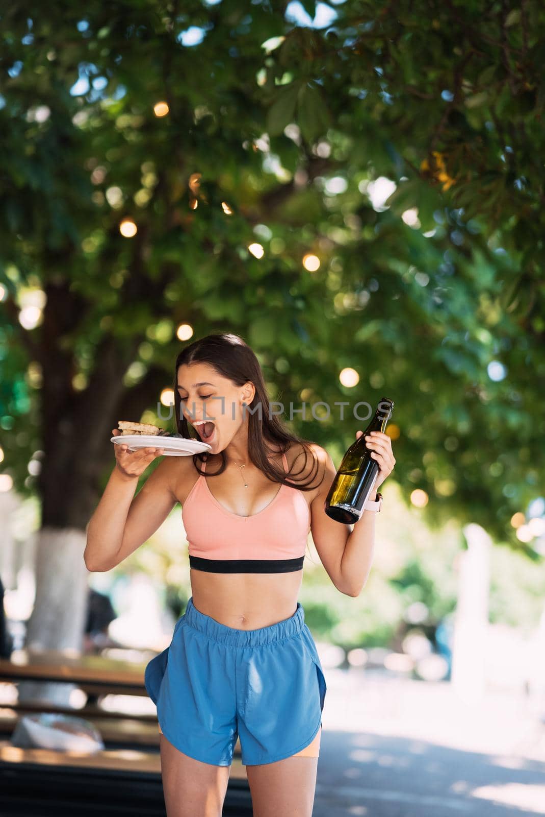 A young woman carries a plate of snacks in one hand and a drink in the other