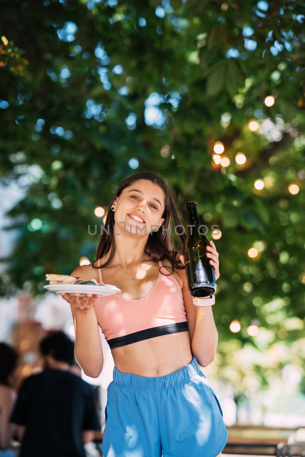 A young woman carries a plate of snacks in one hand and a drink in the other