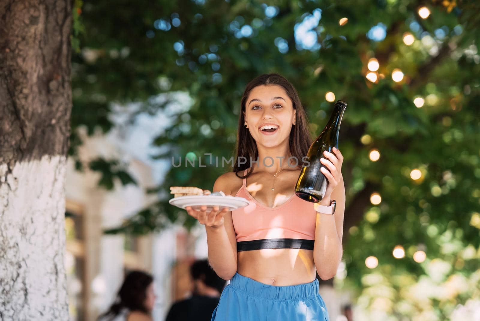 A young woman carries a plate of snacks in one hand and a drink in the other