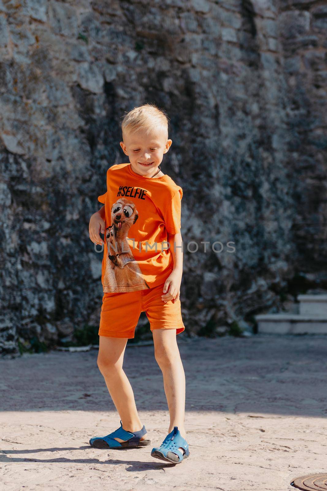 Kid's outdoor activity. Smile toddler boy wearing a orange shorts Jumping, running and having fun in a backyard on a sunny hot summer day. Full length of energetic little boy in stylish casual outfit jumping outdoor. by Andrii_Ko