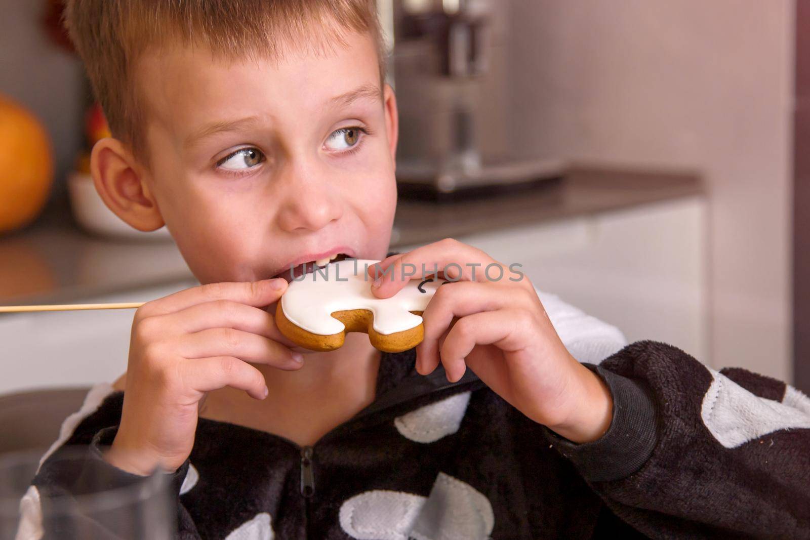 close-up, portrait of a boy in a skeleton costume for a Halloween party. He eats a gingerbread sugar-coated cookie. The concept of a homely cozy holiday for the whole family.